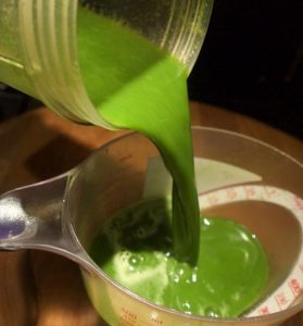 A bright green liquid pours from one container to another.