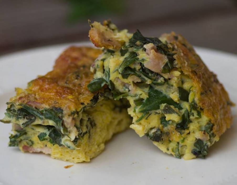 Two slices of a frittata are propped on a plate. The top is golden brown, while green leaves and yellow eggs interleave the inside.