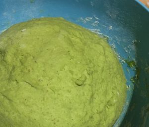 A textured green substance against a blue background. It's bred dough made with warrigal greens, in a blue bowl.