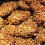 A heap of goldern rough-edged bisuits is sitting on a tray. The rolled oats of a classic ANZAC biscuit are clearly visible.
