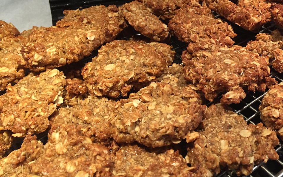 A heap of goldern rough-edged bisuits is sitting on a tray. The rolled oats of a classic ANZAC biscuit are clearly visible.