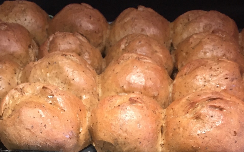 A tray holds glossy brown bread rolls flecked with wattleseed