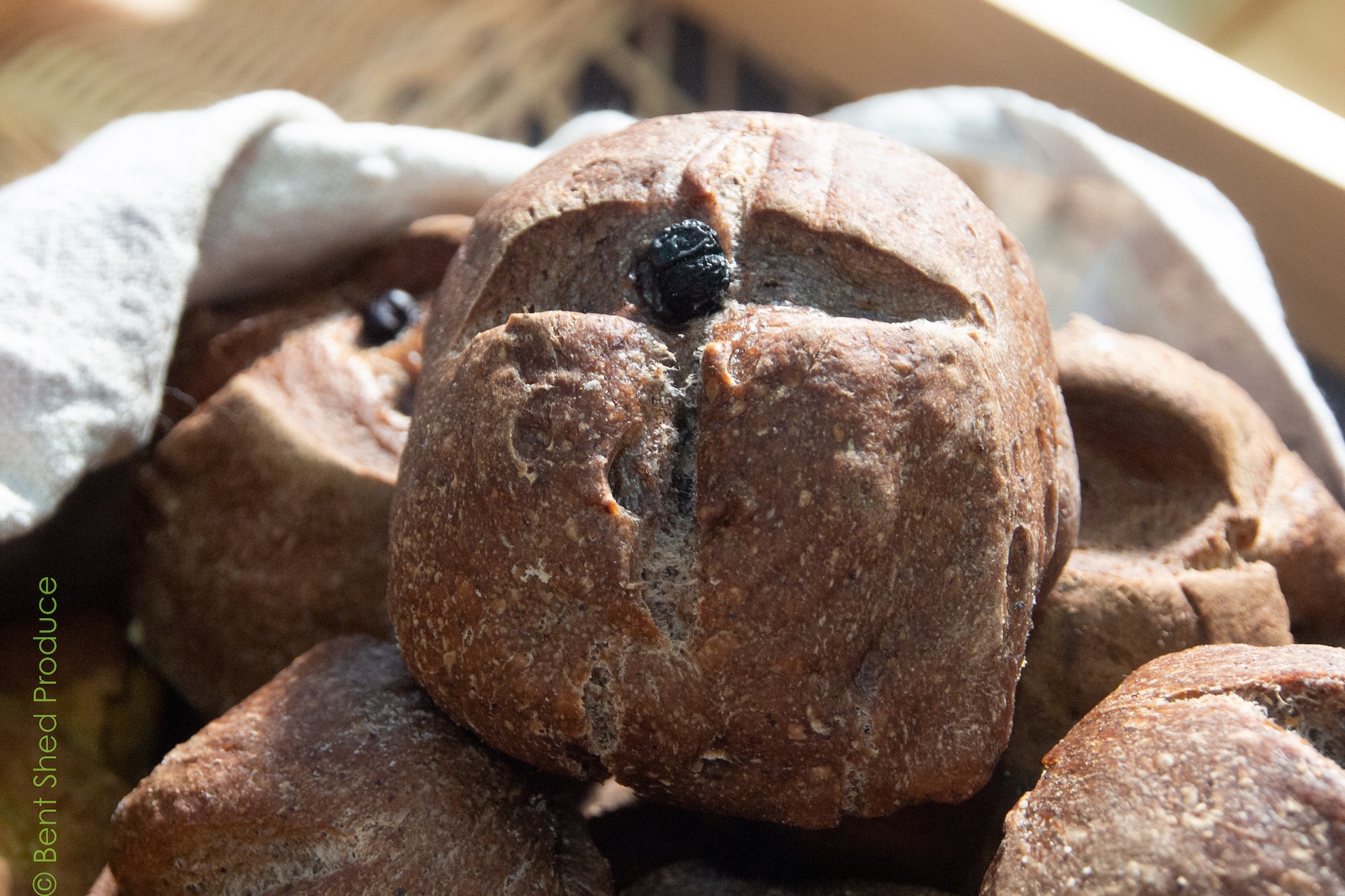 A purplish bread roll sits front and centre of the picture, with a small black berry in the middle of the roll.