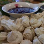 White meringues in the foreground with a blurry bowl of a deep pink sauce behind