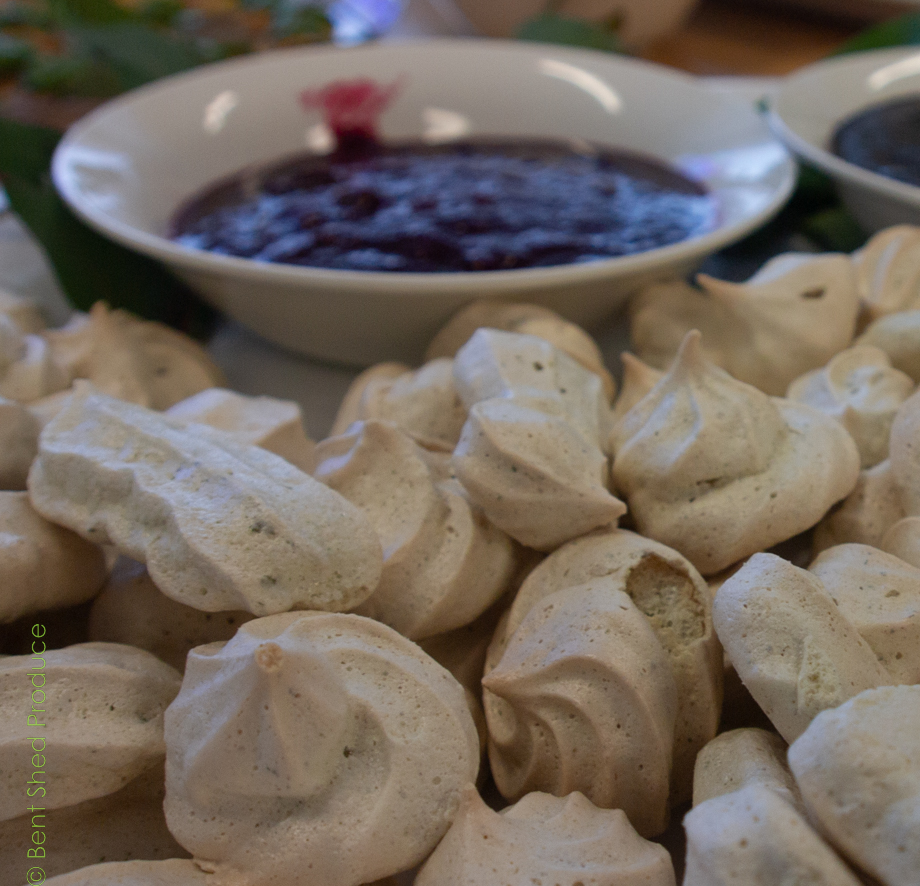 White meringues in the foreground with a blurry bowl of a deep pink sauce behind