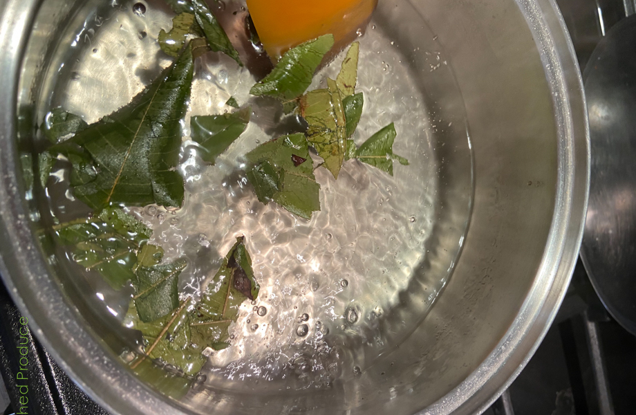Green leaves are in a clear bubbling liquid, inside a silver pot.