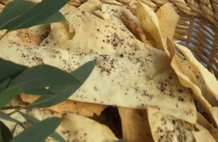 Sheets of white crackers lie in a basket. There are dark flecks scattered on the surface; this is Native Peppersalt. There are green leaves to the left.