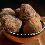Four small balls of dusty brown sit in an orange bowl. They are delicious chocolate truffles with pepperberry.