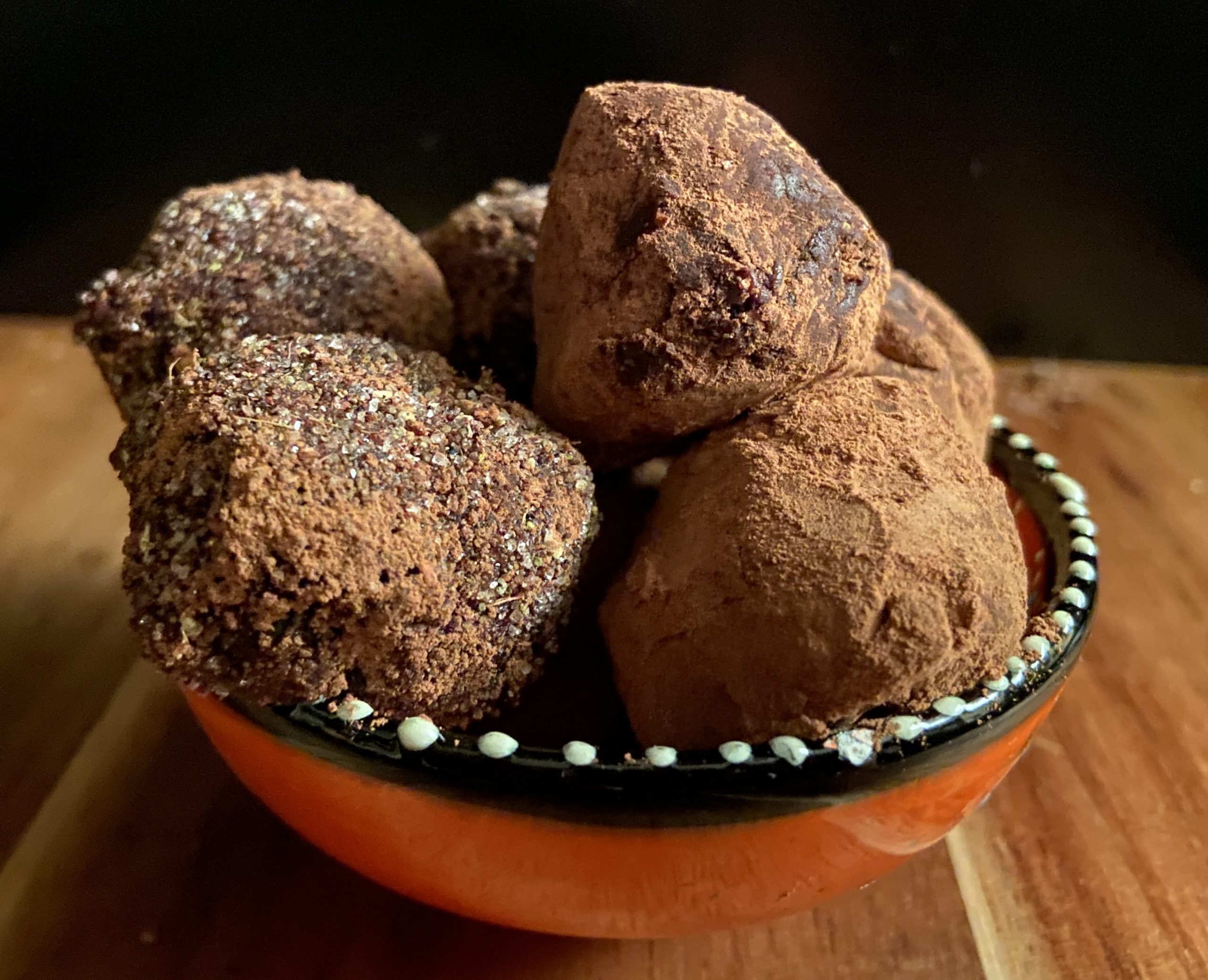 Four small balls of dusty brown sit in an orange bowl. They are delicious chocolate truffles with pepperberry.